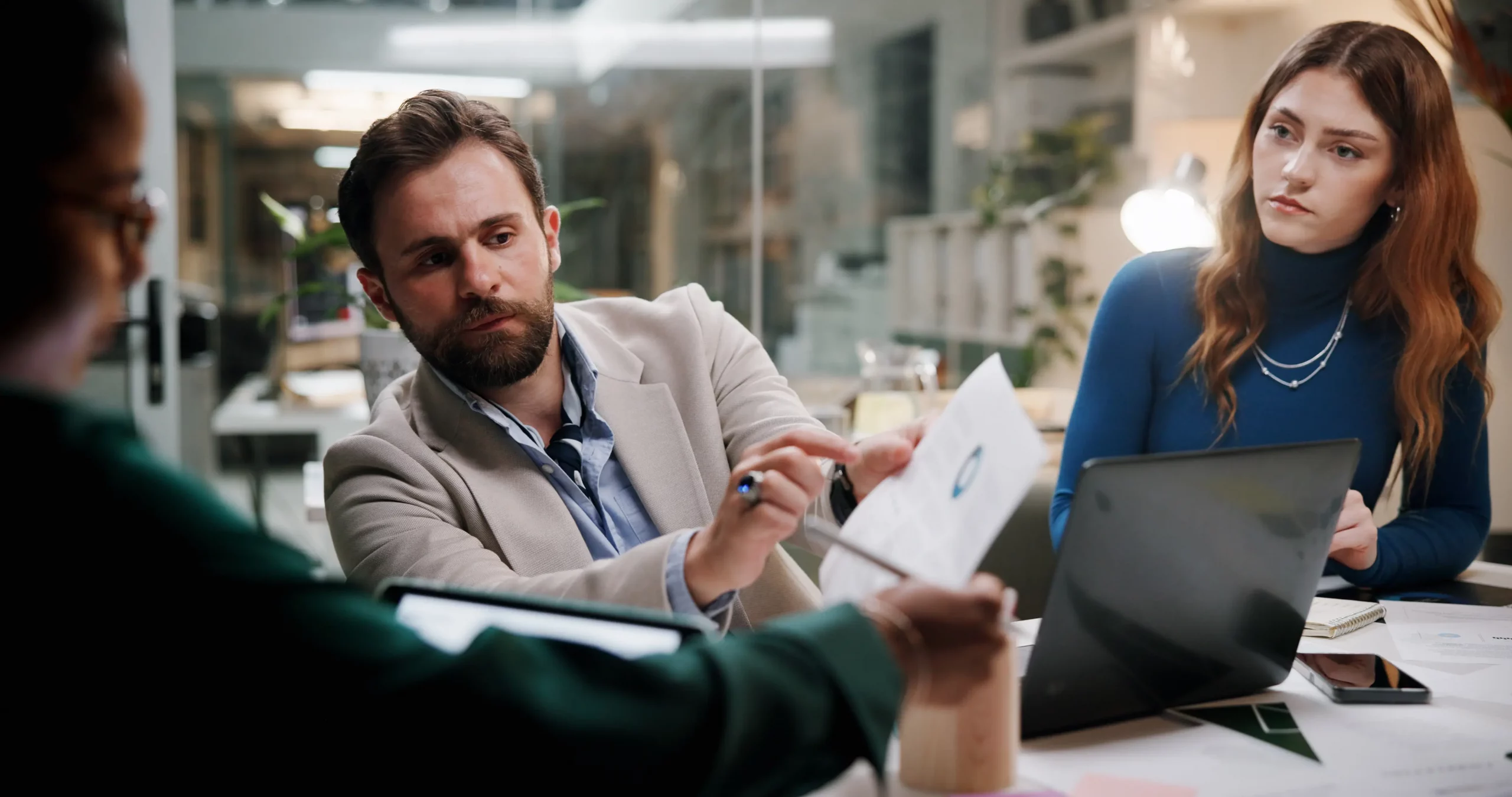 Three professionals in a modern office conducting a disciplinary hearing, with one manager pointing to documents while discussing with colleagues around a table—essential guide on how to conduct a disciplinary hearing fairly and compliantly.