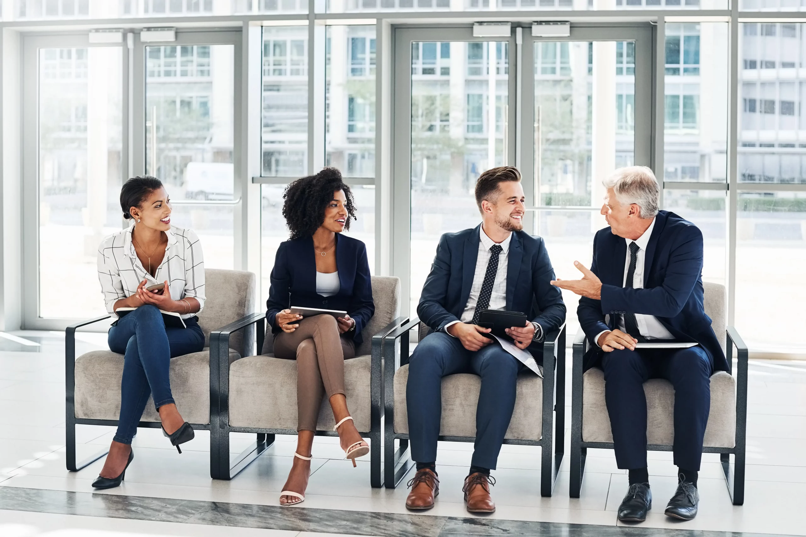 Diverse group of professionals in business attire engaged in a collaborative meeting in a modern UK office lounge, exemplifying how to employ someone in a small business UK through inclusive team dynamics.