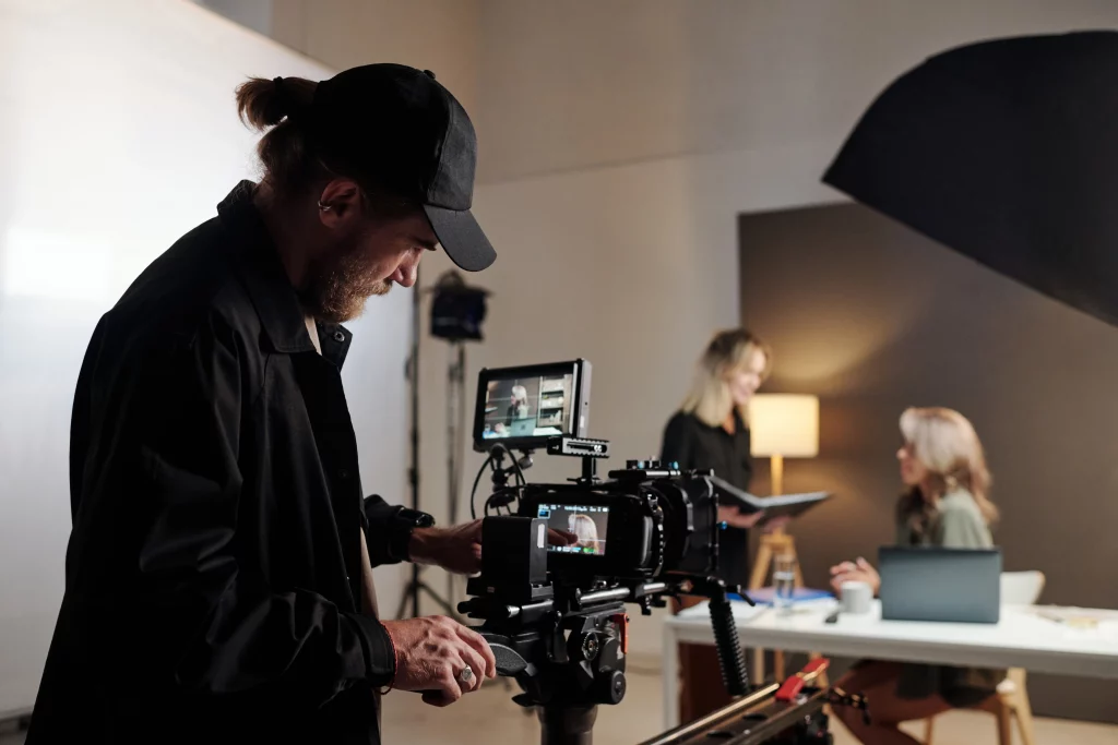 A dynamic behind-the-scenes view of a professional video production team at work, with a videographer adjusting a high-end camera on a tripod while collaborators review footage on a tablet—perfectly capturing when to employ a video production agency for polished B2B results.