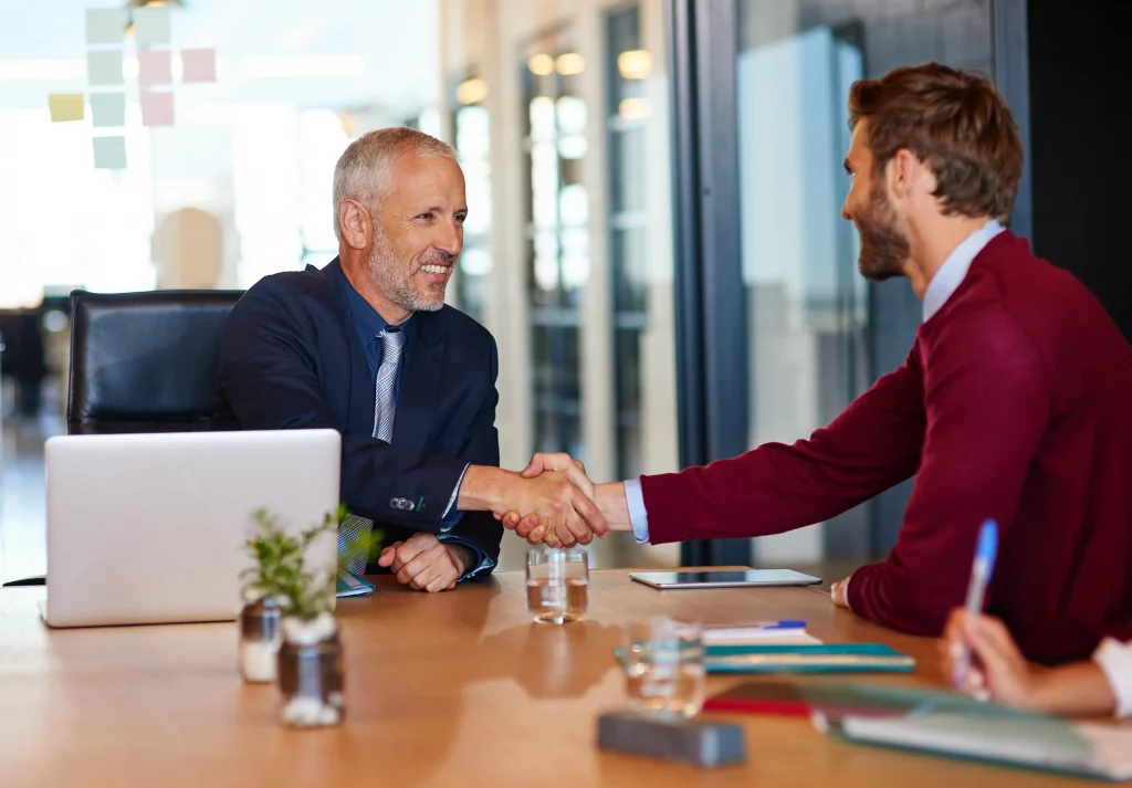 two business men shaking hands at an office desk after discussing what are open and closed questions and learning from it