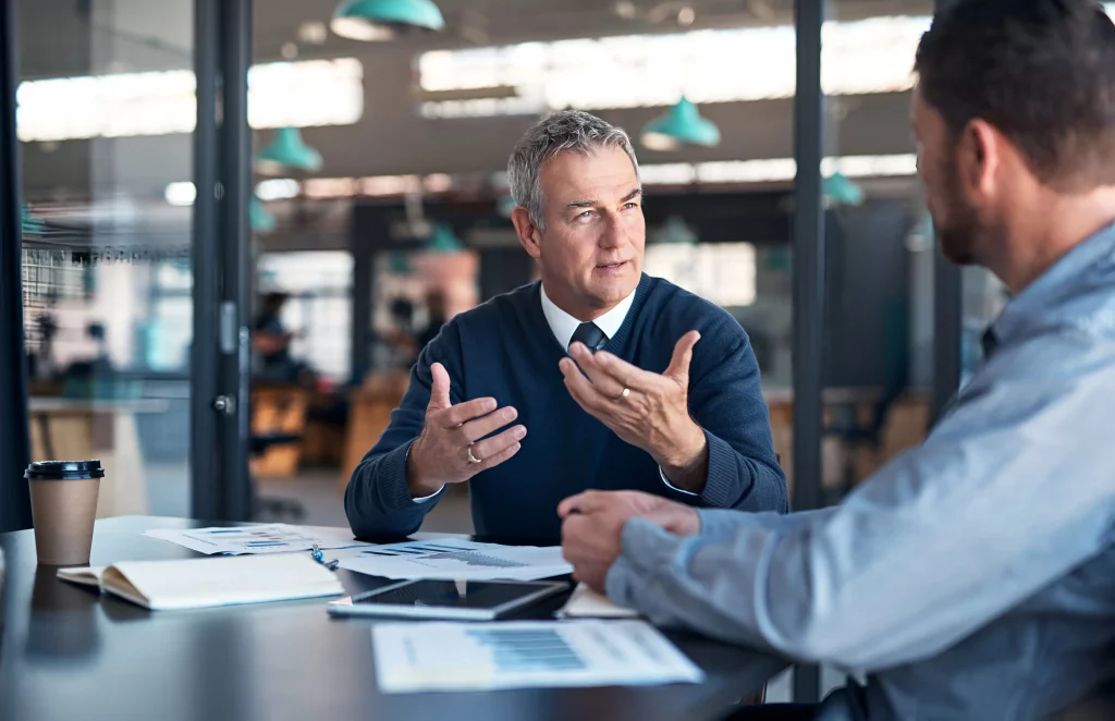 two business people sat at a desk in an office discussing what are open and closed questions