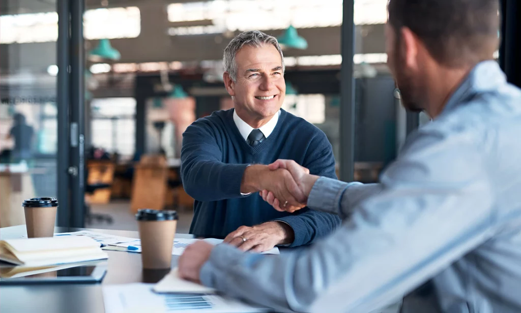Manager welcoming a new team member with a handshake during an onboarding meeting – a key step in how to manage employees in a small business