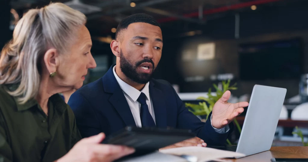 Manager explaining work on a laptop to a colleague in a modern office setting, demonstrating practical ways to manage employees in a small business