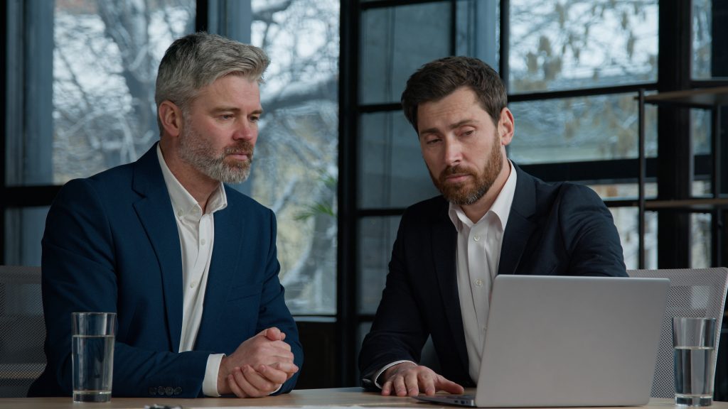 two business men looking at a laptop deciding on the best hr company to partner with to make an employee handbook