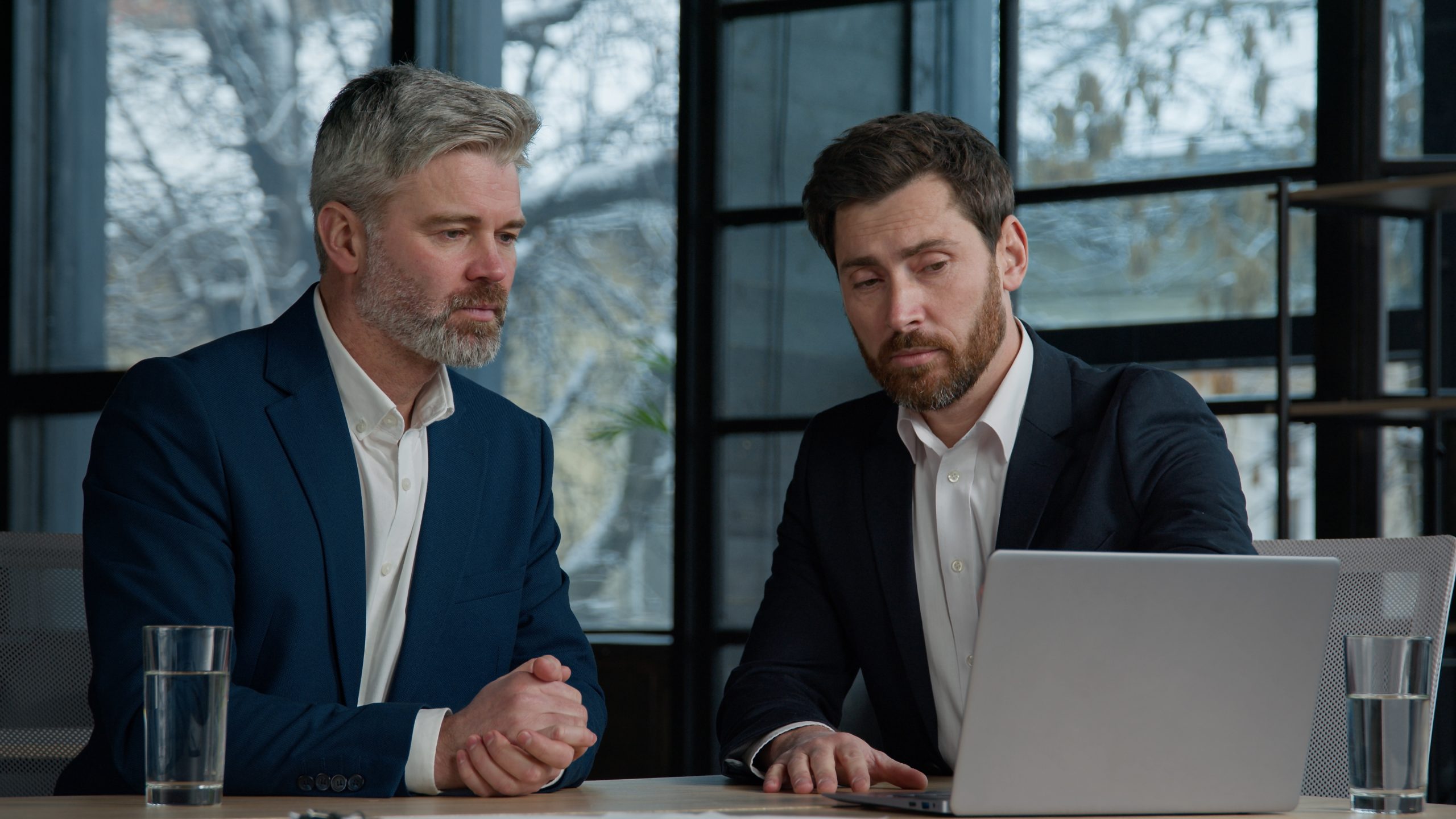 two business men looking at a laptop deciding on the best hr company to partner with to make an employee handbook