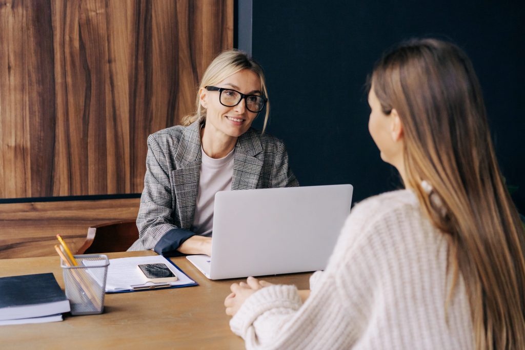 A smiling web designer in glasses and blazer consulting with a client over a laptop in a professional office setting at a mobile responsive web design agency