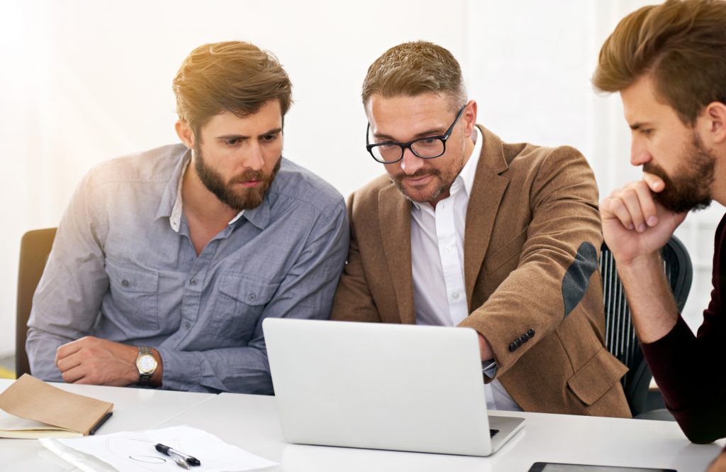 Team of business professionals discussing web design services while gathered around a laptop in a bright office